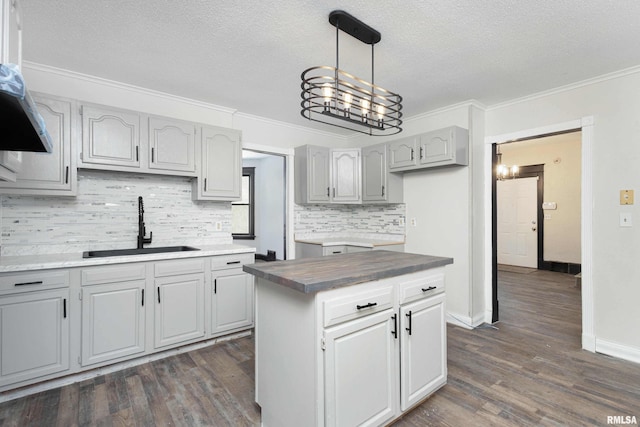 kitchen featuring ornamental molding, dark wood-style flooring, a chandelier, wooden counters, and a sink