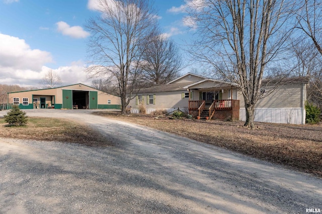 view of front of house featuring a garage, covered porch, dirt driveway, and an outbuilding