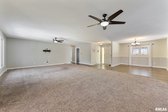 unfurnished living room featuring ceiling fan with notable chandelier, dark colored carpet, a textured ceiling, and baseboards