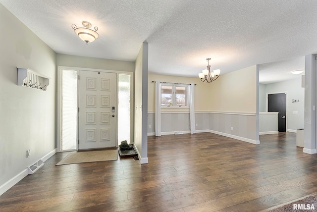 entryway featuring a chandelier, dark wood-type flooring, visible vents, and baseboards