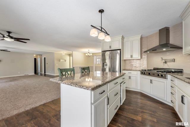 kitchen with stainless steel appliances, open floor plan, wall chimney range hood, a center island, and decorative light fixtures