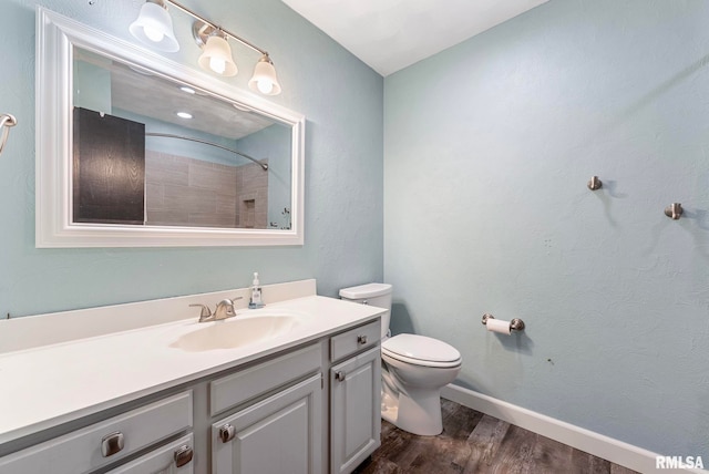 bathroom with a shower, toilet, vanity, wood finished floors, and baseboards