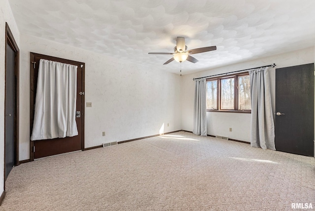 carpeted empty room featuring a ceiling fan, visible vents, and baseboards