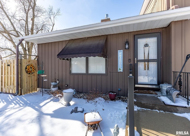 snow covered property entrance featuring board and batten siding and fence