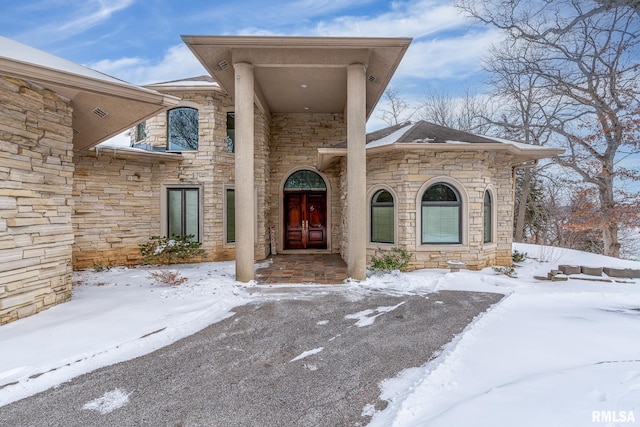 snow covered property entrance featuring stone siding