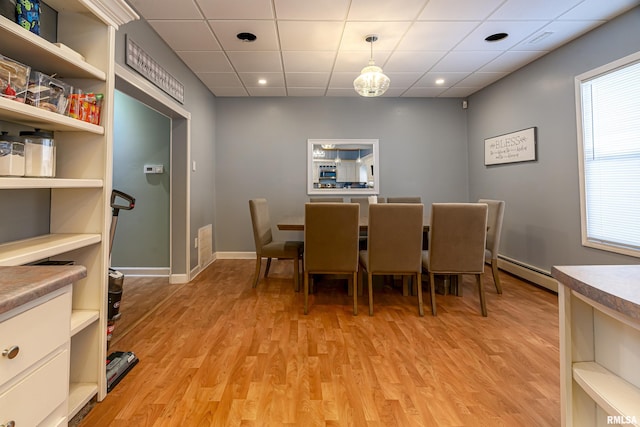 dining space featuring a paneled ceiling, light wood finished floors, baseboards, and baseboard heating