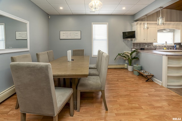 dining space with baseboard heating, a drop ceiling, and light wood-style flooring