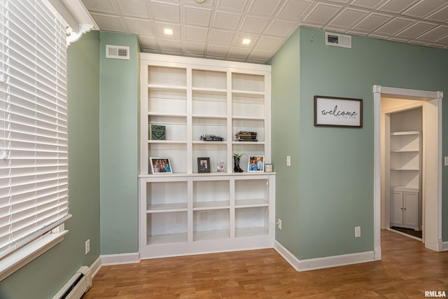 interior space with a baseboard heating unit, an ornate ceiling, baseboards, and wood finished floors