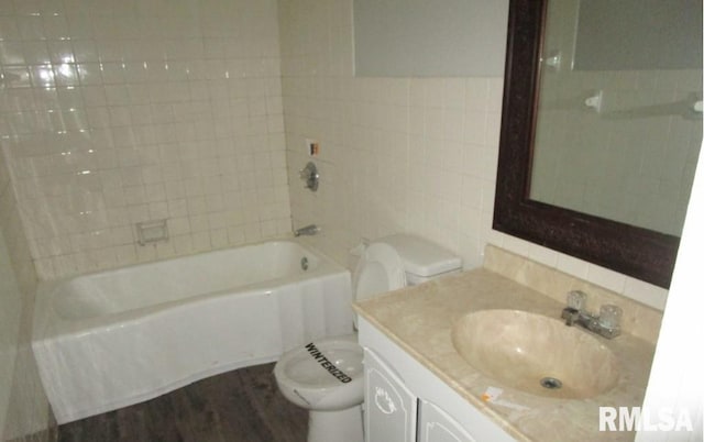 bathroom with shower / bathtub combination, toilet, wood finished floors, vanity, and tile walls