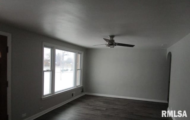 empty room with dark wood-style floors, arched walkways, baseboards, and a ceiling fan