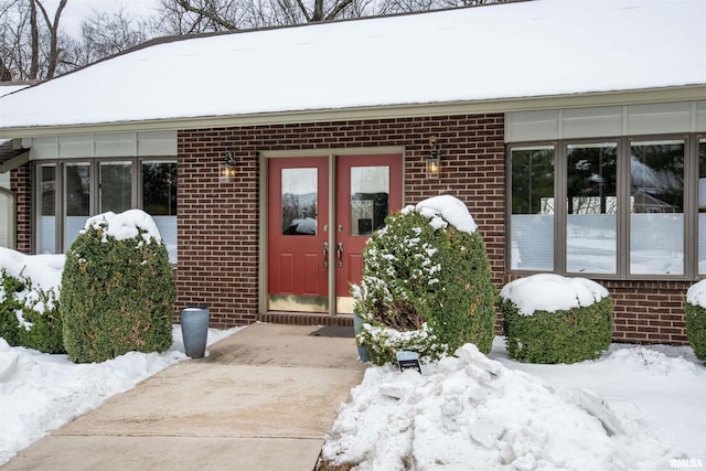 snow covered property entrance with brick siding