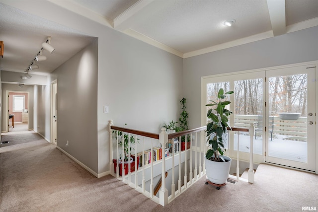 hallway featuring carpet, crown molding, an upstairs landing, track lighting, and baseboards