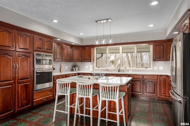 kitchen with stainless steel appliances, a breakfast bar, a sink, light countertops, and tasteful backsplash