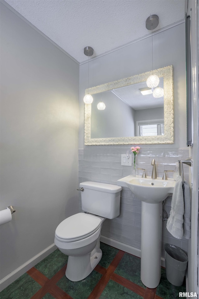 bathroom with toilet, tile walls, baseboards, and a textured ceiling