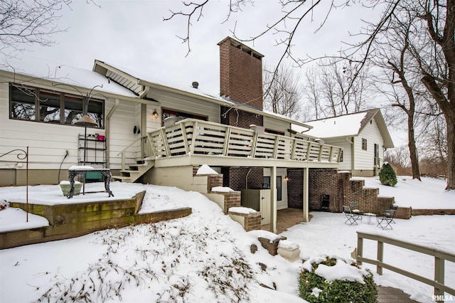 snow covered back of property featuring stairs, a chimney, and a wooden deck