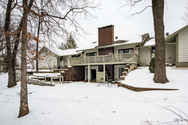 snow covered back of property featuring a deck, a chimney, and stairs