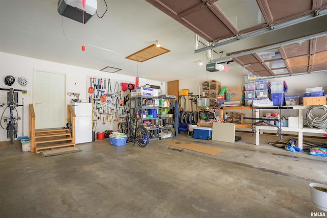 garage with a workshop area, freestanding refrigerator, and a garage door opener