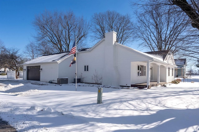 view of snowy exterior with a garage, cooling unit, and a chimney