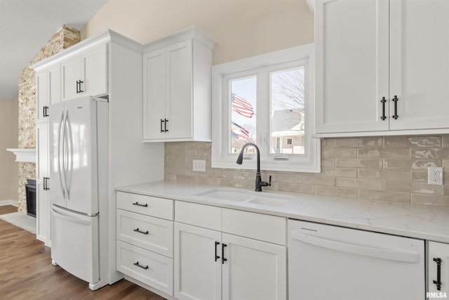 kitchen with white appliances, a fireplace, a sink, white cabinetry, and light stone countertops