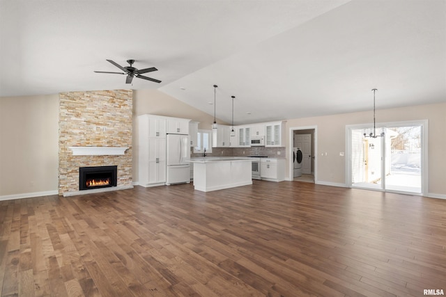 unfurnished living room featuring dark wood-style flooring, lofted ceiling, a stone fireplace, independent washer and dryer, and ceiling fan with notable chandelier