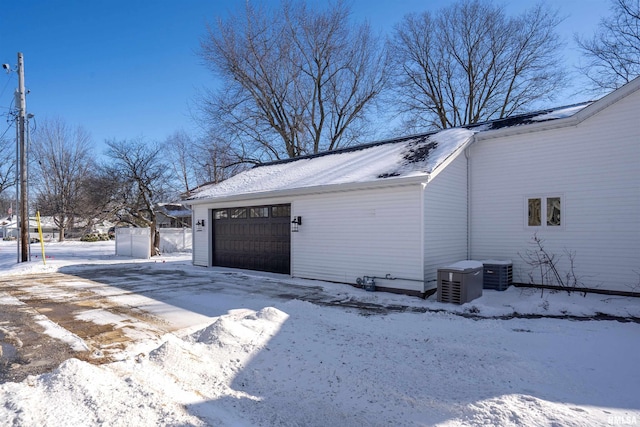 snow covered property with a garage, driveway, and cooling unit