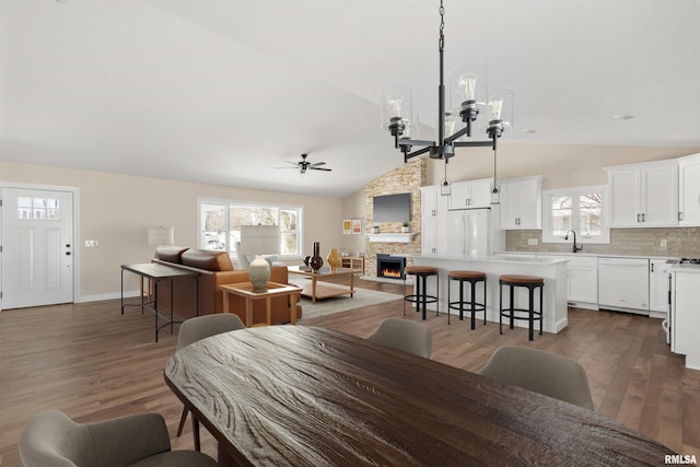 dining space with dark wood-style floors, vaulted ceiling, a fireplace, and ceiling fan with notable chandelier