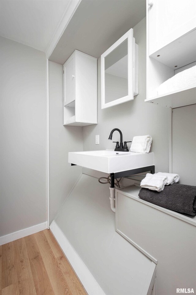 interior space featuring a sink, baseboards, white cabinets, light countertops, and light wood-type flooring