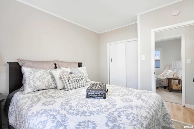 bedroom with a closet, baseboards, crown molding, and wood finished floors