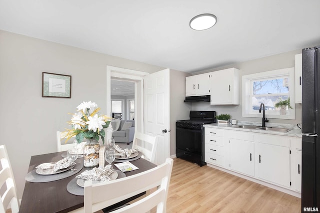 kitchen with under cabinet range hood, light countertops, black appliances, white cabinetry, and a sink