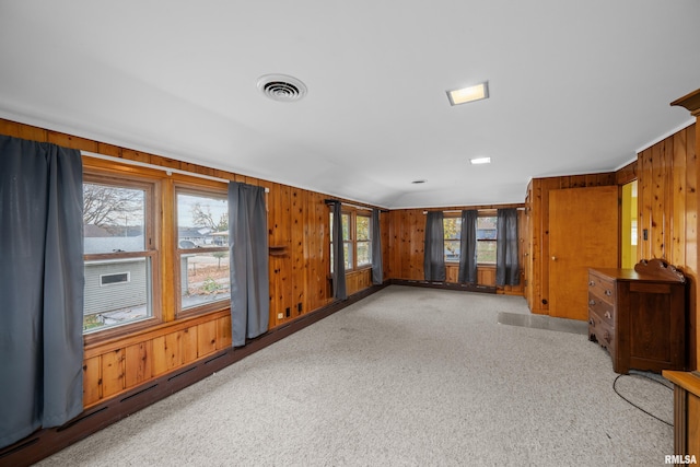 spare room with lofted ceiling, wood walls, visible vents, and light colored carpet