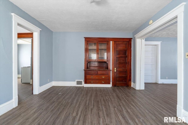 empty room featuring visible vents, baseboards, and dark wood-type flooring