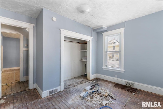 unfurnished bedroom featuring a closet, visible vents, baseboards, and wood finished floors