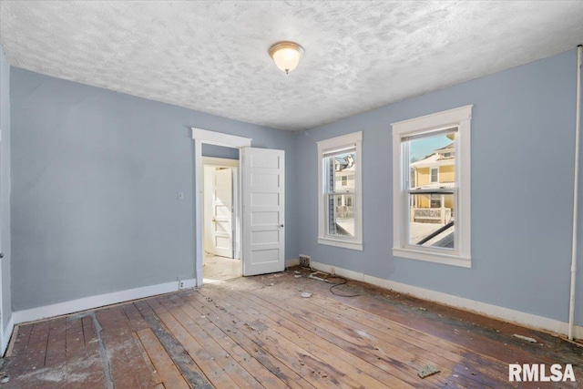 unfurnished room with a textured ceiling, baseboards, and wood finished floors