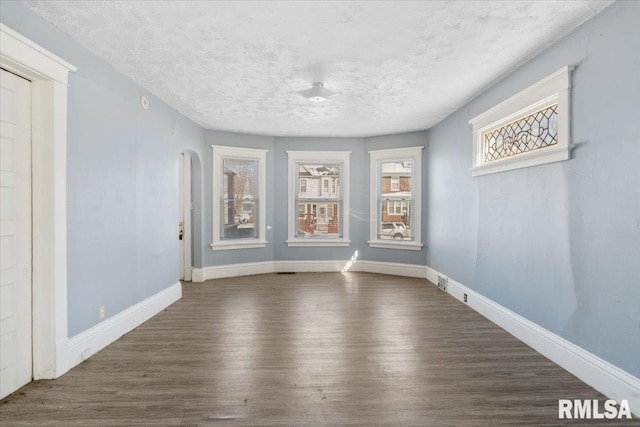 unfurnished room featuring arched walkways, a healthy amount of sunlight, dark wood finished floors, and baseboards