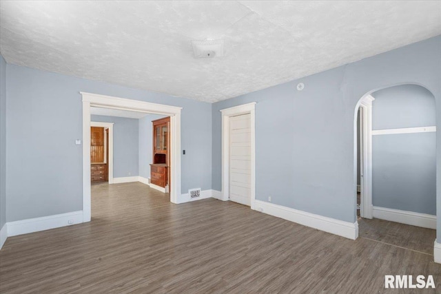 unfurnished room featuring baseboards, arched walkways, and dark wood-style flooring