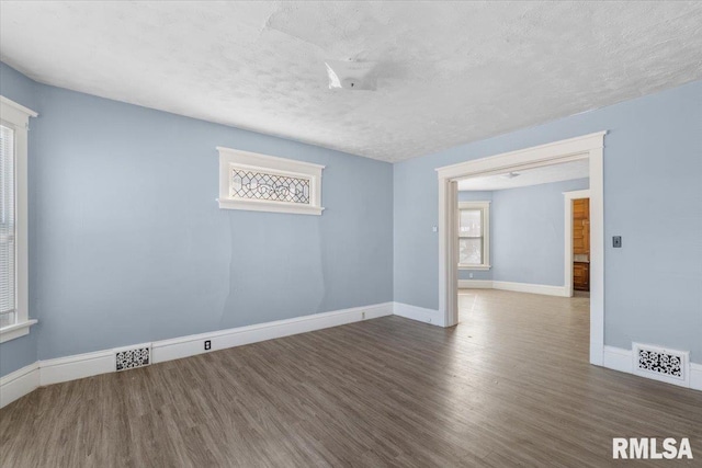 unfurnished room with dark wood-style floors, baseboards, visible vents, and a textured ceiling