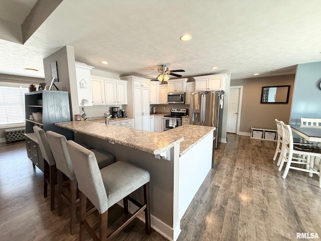 kitchen with a breakfast bar, wood finished floors, a peninsula, stainless steel appliances, and a textured ceiling