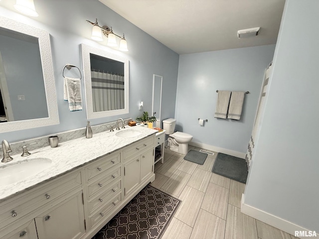 full bathroom with baseboards, a sink, toilet, and double vanity