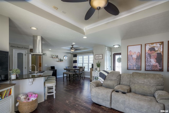 living room with a tray ceiling, dark wood-style flooring, recessed lighting, ornamental molding, and baseboards