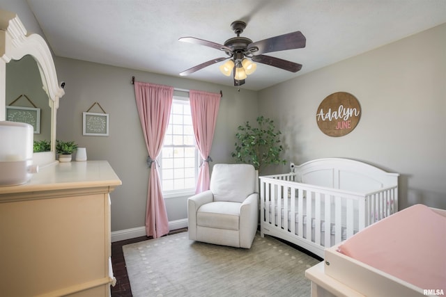 bedroom featuring a nursery area, ceiling fan, baseboards, and wood finished floors