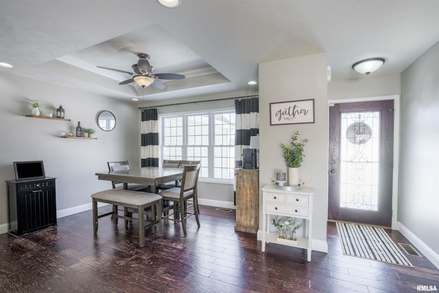 dining space with dark wood-style floors, a tray ceiling, visible vents, and baseboards