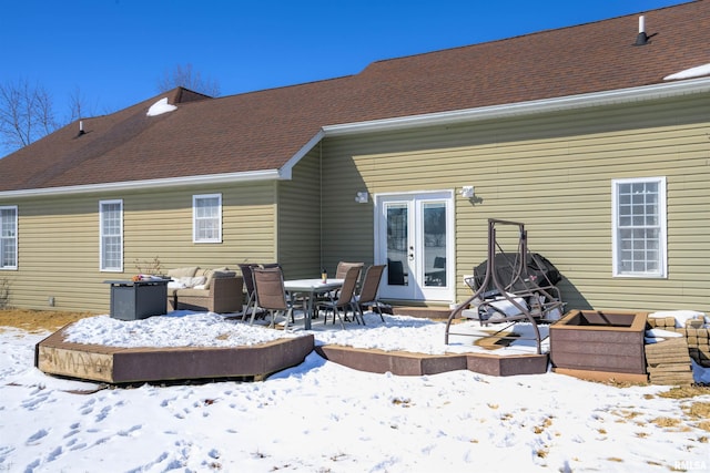 snow covered back of property with french doors and roof with shingles