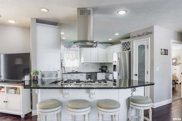 kitchen with dark wood-style flooring, island exhaust hood, appliances with stainless steel finishes, white cabinetry, and a peninsula