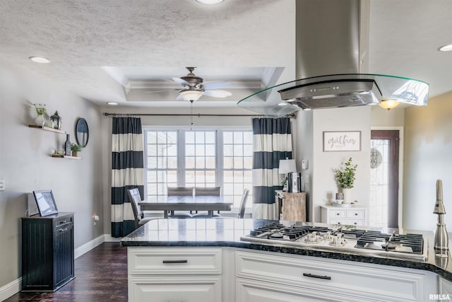 kitchen with stainless steel gas cooktop, island exhaust hood, dark countertops, white cabinetry, and a textured ceiling