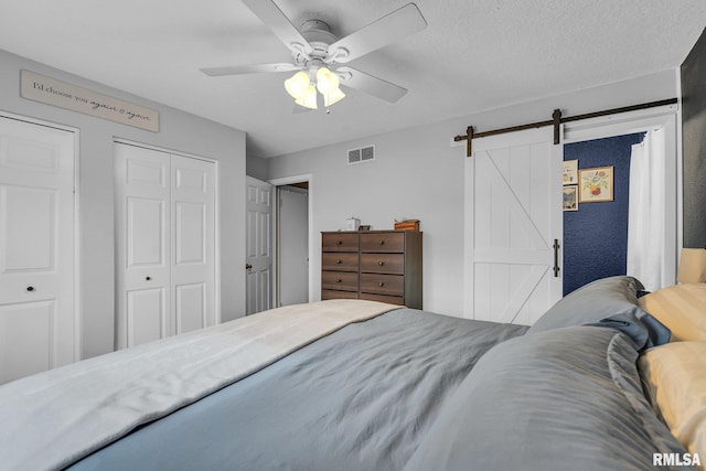 bedroom with a ceiling fan, visible vents, a textured ceiling, and a barn door