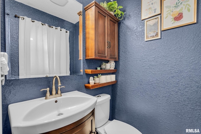 bathroom featuring toilet, a sink, and a textured wall