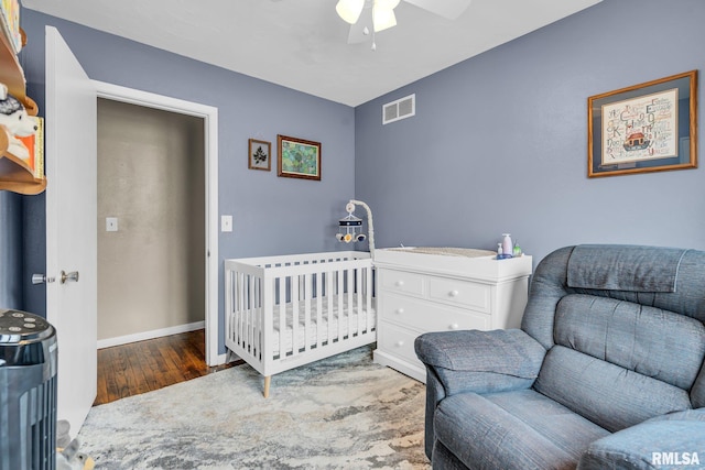 bedroom with visible vents, a ceiling fan, wood finished floors, a crib, and baseboards