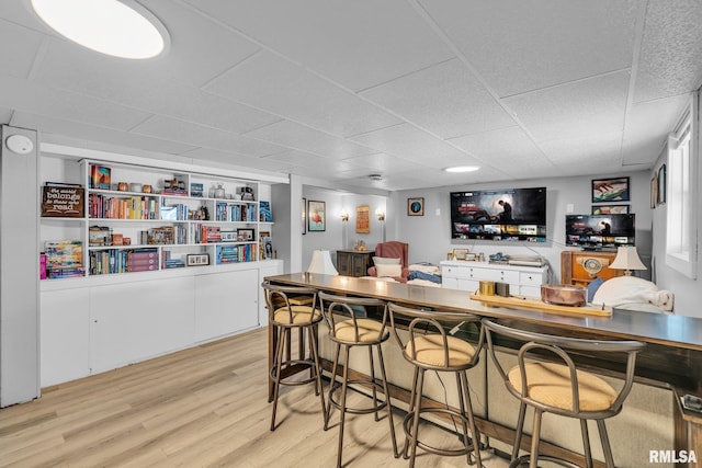 bar featuring light wood-style floors, a paneled ceiling, and bar area