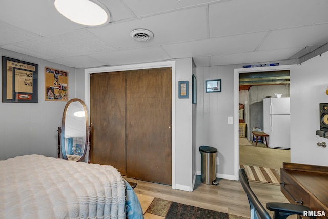 bedroom with visible vents, a drop ceiling, freestanding refrigerator, light wood-type flooring, and a closet