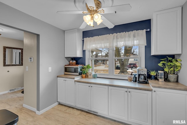 kitchen featuring light countertops, stainless steel microwave, visible vents, white cabinets, and ceiling fan